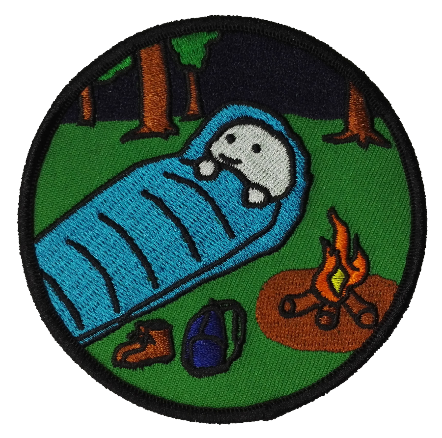 Embroidered patch of a cartoon character sleeping in a blue sleeping bag with a campfire and backpack in a forest setting.