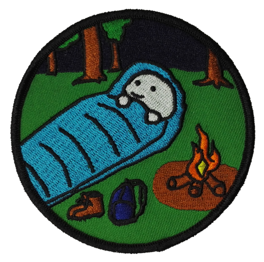 Embroidered patch of a cartoon character sleeping in a blue sleeping bag with a campfire and backpack in a forest setting.